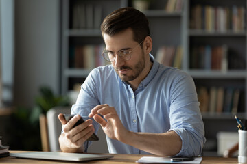 Wall Mural - serious businessman wearing spectacles using mobile phone sit at desk in cozy office. manager solve 