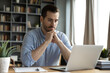 © fizkes - Young businessman sit at home office desk looks at laptop read media news online, learn new e app, analyzing project, stuck with challenge business task, thinks over problem, search solution concept