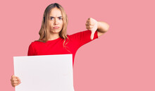 Young Beautiful Blonde Woman Holding Blank Empty Banner With Angry Face, Negative Sign Showing Dislike With Thumbs Down, Rejection Concept