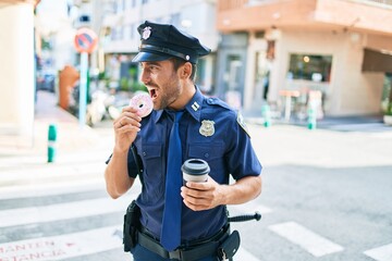 Poster - Young handsome hispanic policeman wearing police uniform smiling happy. Eating donut and drinking cup of take away coffee at town street.