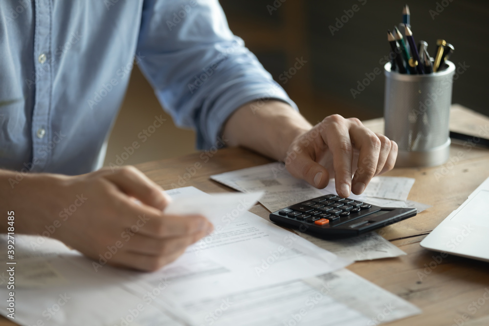 Personal finance management, accounting concept. Close up view man sitting at table using calculator performs arithmetic operations calculates costs per month, manage family budget, control expenses - obrazy, fototapety, plakaty 