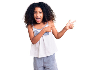 African american child with curly hair wearing casual clothes smiling and looking at the camera pointing with two hands and fingers to the side.