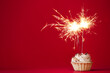Cupcake with burning sparkler on red background. Space for text