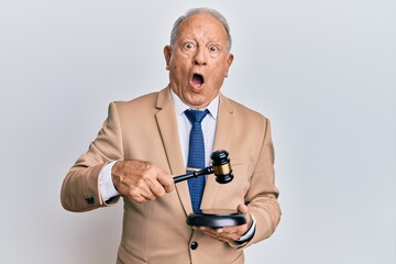 Poster - Senior caucasian judge man using gavel in shock face, looking skeptical and sarcastic, surprised with open mouth