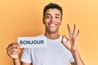 © Krakenimages.com - Young handsome african american man holding bonjour french greeting word doing ok sign with fingers, smiling friendly gesturing excellent symbol