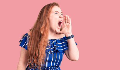 Poster - Young beautiful redhead woman wearing casual clothes shouting and screaming loud to side with hand on mouth. communication concept.