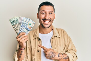 Wall Mural - Handsome man with tattoos holding dollars smiling happy pointing with hand and finger