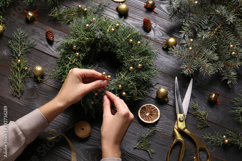 Fotografía Florist making beautiful Christmas wreath at black wooden table, closeup