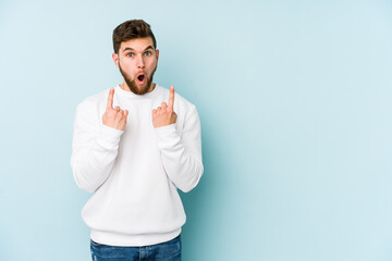 Wall Mural - Young caucasian man isolated on blue background pointing upside with opened mouth.