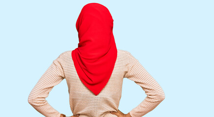 Young african american woman wearing traditional islamic hijab scarf standing backwards looking away with arms on body