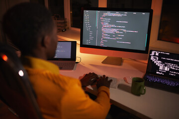 back view portrait of african-american man writing code while working with multiple computer screens