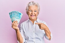 Senior Grey-haired Woman Holding 100 Brazilian Real Banknotes Smiling Happy Pointing With Hand And Finger