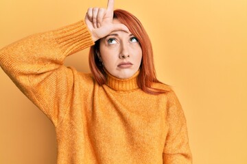 Wall Mural - Beautiful redhead woman wearing casual winter sweater over yellow background making fun of people with fingers on forehead doing loser gesture mocking and insulting.