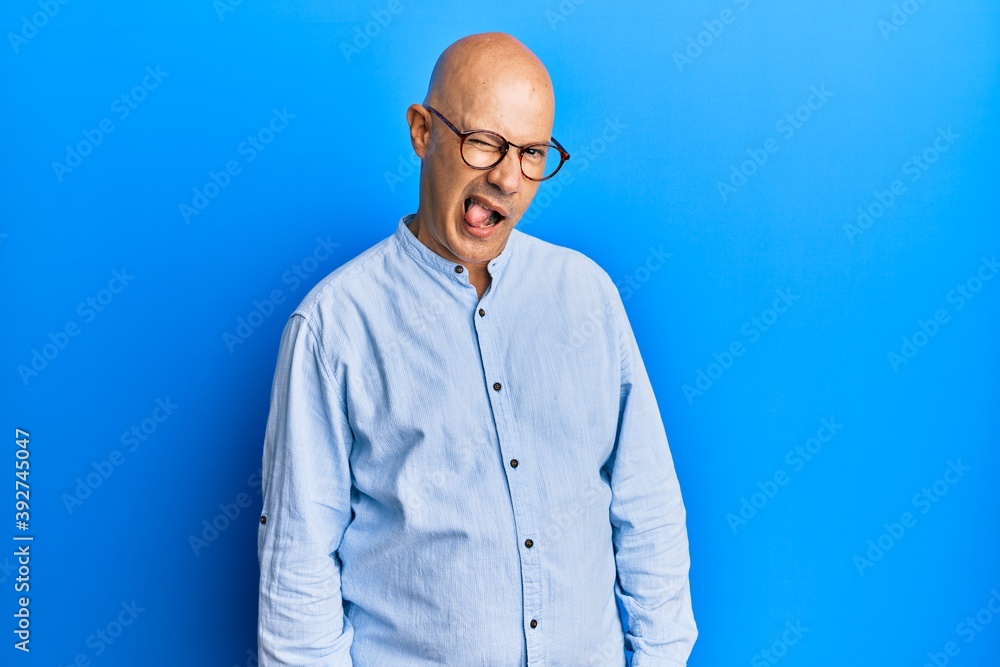 Middle age bald man wearing casual clothes and glasses winking looking at the camera with sexy expression, cheerful and happy face.