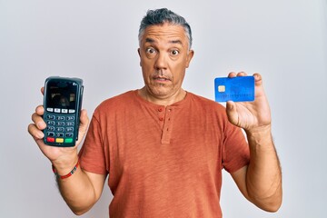 Poster - Handsome middle age mature man holding dataphone and credit card clueless and confused expression. doubt concept.