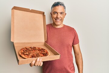 Poster - Handsome middle age mature man holding delivery pizza box looking positive and happy standing and smiling with a confident smile showing teeth