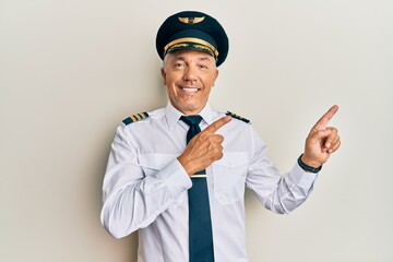 Poster - Handsome middle age mature man wearing airplane pilot uniform smiling and looking at the camera pointing with two hands and fingers to the side.