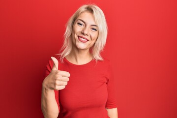 Young blonde girl wearing casual clothes doing happy thumbs up gesture with hand. approving expression looking at the camera showing success.