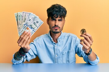 Wall Mural - Young hispanic man holding dollars and bitcoin skeptic and nervous, frowning upset because of problem. negative person.