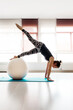 Young active woman leaning on the floor by stretched arms with legs on ball during workout in gym