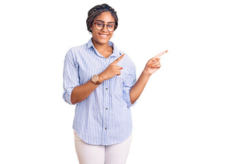 Canvas Print - Young african american woman with braids wearing casual clothes and glasses smiling and looking at the camera pointing with two hands and fingers to the side.