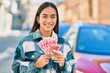 Young latin girl smiling happy holding chinese yuan banknotes at the city.