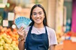 © Krakenimages.com - Young latin shopkeeper girl smiling happy holding brazil real banknotes at the fruit store.