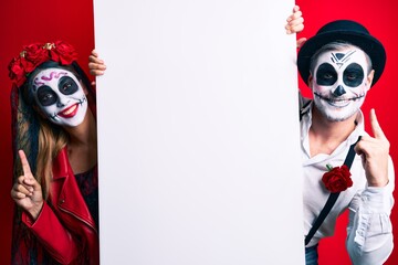 Poster - Couple wearing day of the dead costume holding blank empty banner surprised with an idea or question pointing finger with happy face, number one