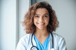 © Stock 4 You - Close-up of happy young female doctor wear blue uniform, white medical coat, stethoscope and looking at camera in hospital office. Portrait of beautiful Hispanic female doctor, therapist, nurse.