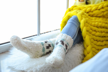 Beautiful young woman in warm socks and with plaid sitting on window sill, closeup