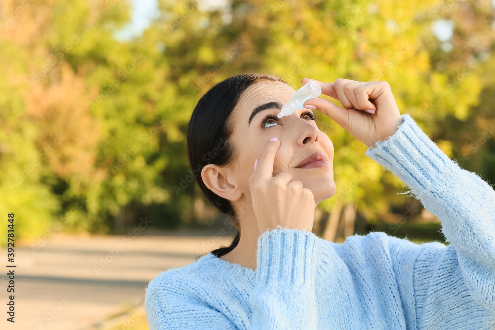 Young allergic woman using eye drops outdoors
