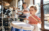 Portrait of small girl indoors at home, playing drums.