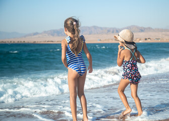 Wall Mural - Two little girls play along the beach by the sea.