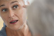 © goodluz - Mature white-haired woman checking eye wrinkles in front of mirror
