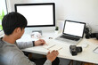 © Prathankarnpap - A graphic designer or photographer is taking note while sitting in front of multiple computer at workplace.