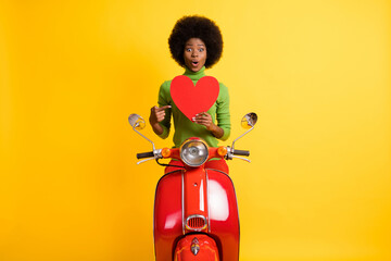 Sticker - Photo portrait of young happy excited african american bike rider woman pointing finger at big red heart card isolated on vivid yellow colored background