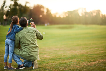 Adorable little girl having fun with soap bubbles on a sunny day, daughter and dad spending time together outdoors