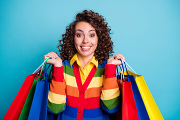 Poster - Photo of beautiful brown curly haired cheerful young woman raise shopping bag wonderful bargain isolated on blue color background