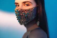 Pandemic Fashion. Quarantine Jewelry. Festive Look. Covid-19 Trend 2021. Portrait Of Confident Woman In Glamour Gold Chain Face Mask With Turquoise Beads On Blur Blue White Color Gradient Background.