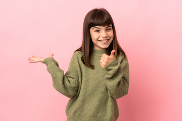 Little girl isolated on pink background holding copyspace imaginary on the palm to insert an ad and with thumbs up