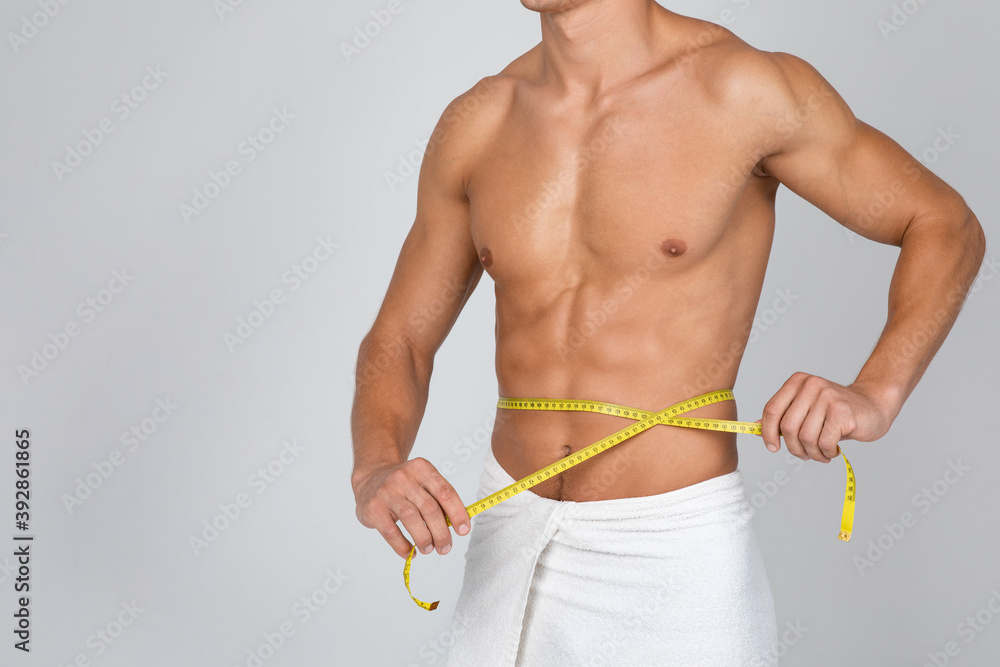 Muscular man measuring his waist with yellow tape - obrazy, fototapety, plakaty 