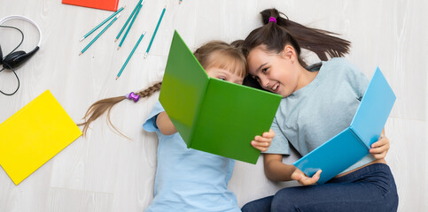 Wall Mural - family, leisure and childhood concept - happy sisters lying on floor and drawing and doing homework at home