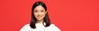 happy and young asian woman in sweater looking at camera isolated on red, banner