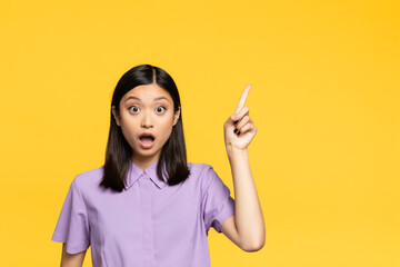 shocked asian woman with open mouth pointing with finger isolated on yellow