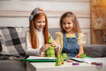 Cheerful. Two little children, girls together in creativity of the house. Happy kids make handmade toys for games or New Year celebration. Little caucasian models. Happy childhood, Christmas