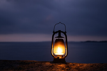 Wall Mural - Beautiful old rustic oil lamp silhouette on the rock in a beautiful sea backgroud. Night time. Light in the dark and hope concept. 