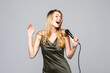 Portrait of female singer wearing evening dress and keeping microphone on grey background. Concept of music