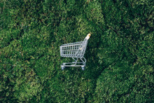 Shopping Cart On Green Grass, Moss Background. Top View. Minimalism Style. Creative Design. Shop Trolley. Sale, Discount, Shopaholism, Ecology Concept. Sustainable Lifestyle, Conscious Consumption