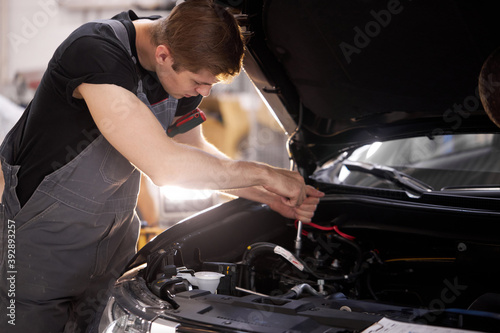 handsome guy repairing auto\'s hood, using tools. wearing unifrom, concentrated on work