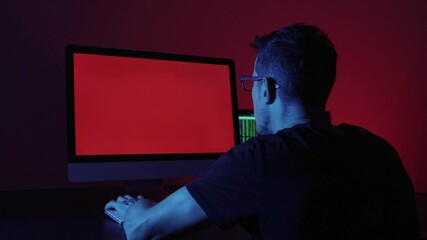 Man typing in front of a computer in a dark office. The Error signal appears on the screen, he hits the keyboard and the table in anger. Concept of frustration and helplessness with technology.